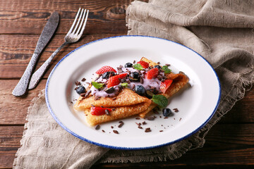 Russian and Ukrainian cuisine. Pancakes with with yogurt and fresh berries: blueberries, strawberries and mint on a white plate on a wooden background. Rustic. Burlap, fork and knife