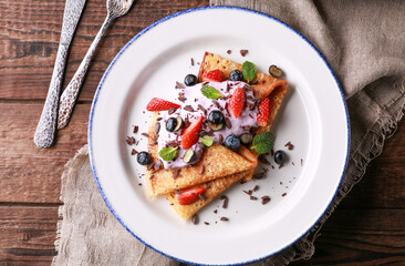 Russian and Ukrainian cuisine. Pancakes with with yogurt and fresh berries: blueberries, strawberries and mint on a white plate on a wooden background. Rustic. Burlap, fork and knife.Flatlay, top view
