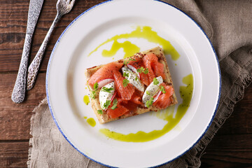 Russian and Ukrainian cuisine. Pancakes with sour cream, salmon, red fish on a white plate on a wooden background. Rustic. Burlap, fork and knife. Traditional dish. Background image. Flatlay, top view