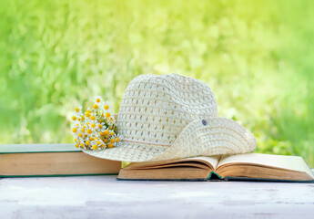 Chamomile flowers, book and summer hat in sunny garden, natural background. relax time, summer season concept. Rustic composition