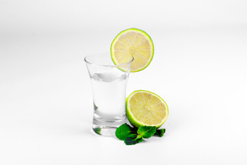 Glass with transparent alcohol liquid, lime and mint leaves isolated on white background.