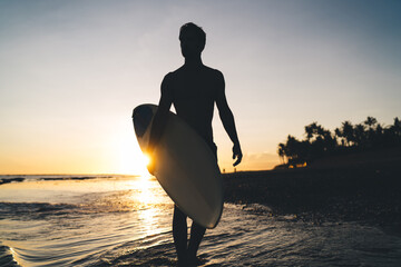 Silhouette of male spending evening for surfing during summer twilight at Carribean sea, amateur...