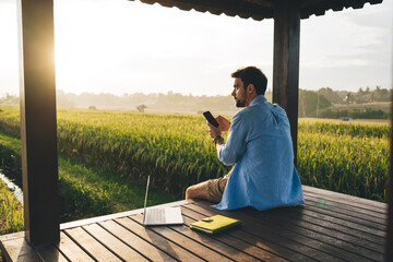 Pondering man browsing smartphone and laptop in field