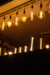 Row of different electric retro hanging lamp bulbs. Dark background. Warm yellow light