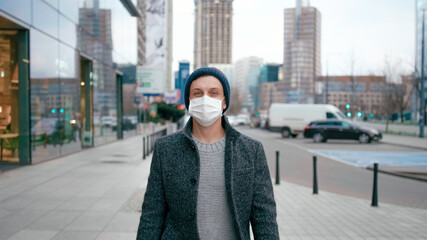 COVID-19 Coronavirus Pandemic or Smog Background. Confident Man in Surgical Face Mask Walks in City Street and Looks to Camera in Winter or Spring.