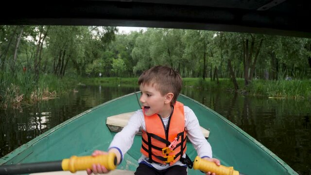 Development child rowing oars on a boat a lake park city. Kid rides a boat with paddle. Recreation children's camp during school holidays. Boy rowing boat children. Kid float on a boat river city park