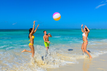 Three young beautiful people playing on the beach with a beach ball, interracial, black