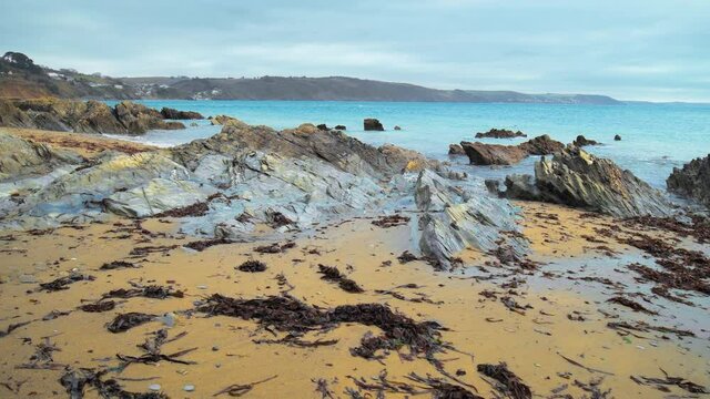 Smooth walk on a Rocky seashore beach with sand and blue water during evening. St Michael's Chapel Of Lammana in Looe, Cornwall, England in 4K. 