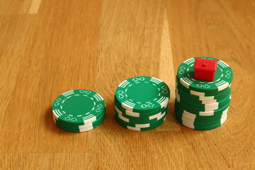 Three piles of poker chips. Green markers with a small red house or hotel on top. Close up and isolated against a wooden background. Concept of winning.