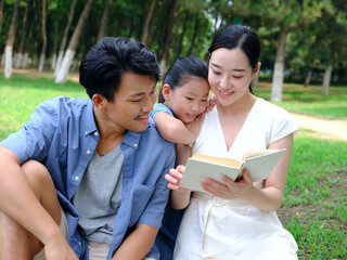A happy family of three is reading outdoors
