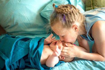 Adorable boy in the bedroom with his older sister. A newborn baby and his sister in a blue-colored bed. Textiles and bedding for children. Family morning at home. Selective focus.