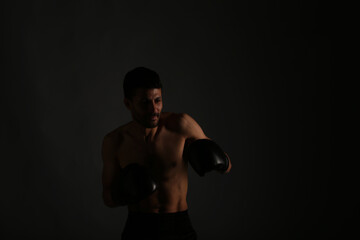 Fototapeta na wymiar Young strong boxer fighting in shadows