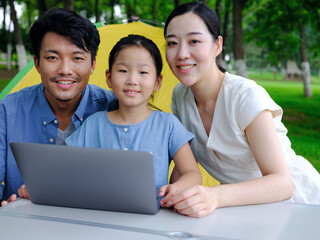 Happy family of three use computer to surf the Internet outdoors