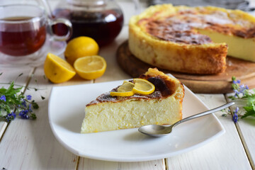 Sweet snack: a slice of cheese pie with lemon on a nice plate, a cheese pie and a cup of tea on a white table