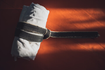 White kimono tied with a black belt on an orange tatami in a martial arts hall. Place for text.