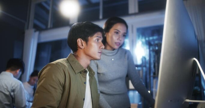 Young Asian business man and woman work late night together on desktop computer with team in home office. Project brainstorm meeting, Small business startup, coworker cooperate teamwork concept