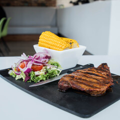 Steak with side salad and corn on the cob.