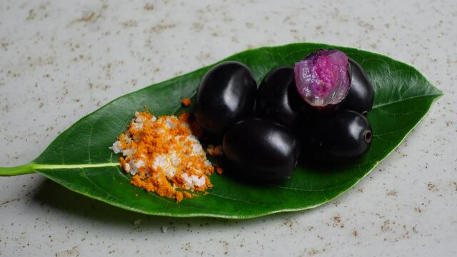 Spicy mixed salt with some black java plum fruit in the green leaves. A way to eat ripe cesium camini fruit by hand. 4k closeup video.