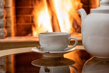 Cozy Fireplace scene, white cup of tea and teapot on a table.
