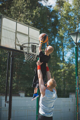 Happy family playing basketball. Young sportive father with son in hands. Kid boy throwing ball in basketball hoop