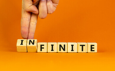 Finite or infinite symbol. Businessman turns wooden cubes and changes the word 'finite' to 'infinite'. Beautiful orange table, orange background. Business, finite or infinite concept. Copy space.