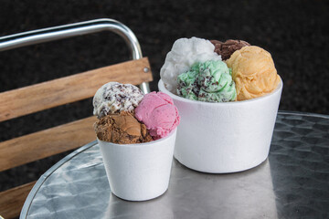 Large and small isopor containers with different flavors of ice cream on a metal table.
