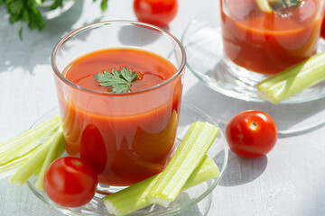 Two glasses with fresh tomato juice, celery, parsley and ripe tomatoes on light wood background.