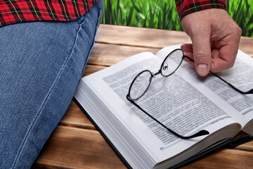A man sitting on a bench in nature reads a book.
