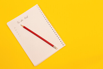 Notepad and pencil lie on yellow background with copy space
