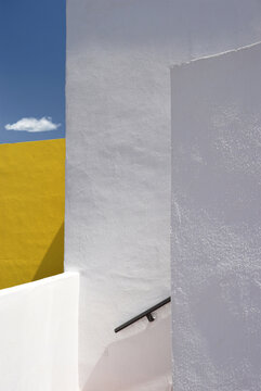 Minimalist surreal architectural composition with white and yellow walls on the blue sky and a lonely cloud background, Spain, Andalusia, bright sunlight