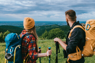 A young couple of hikers using trekking poles and wearing backpacks