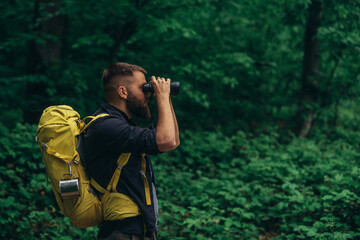 A hiker man walking in the forest and using binoculars