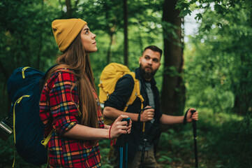 A young couple of hikers using trekking poles and wearing backpacks