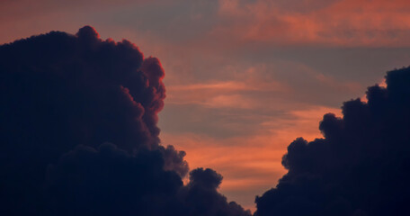 Dramatic orange sky between dark thick clouds that are illuminated by the red sunset and hid behind the clouds.