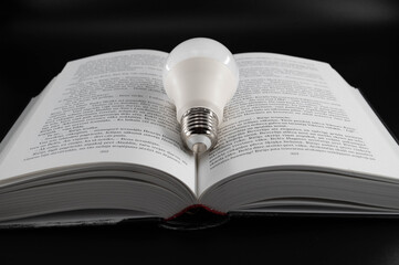Fototapeta premium Led bulb in the middle of an open book on an isolated black background.
