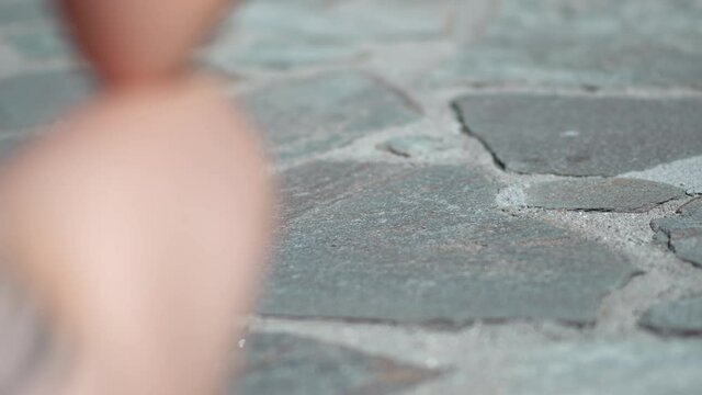 Baby legs make first steps on patterned paving tiles, cement brick floor, slow motion