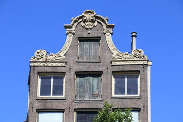 Fototapeta na wymiar Amsterdam Oudezijds Voorburgwal Canal Old House Facade Detail with Bell Gable Against a Blue Sky