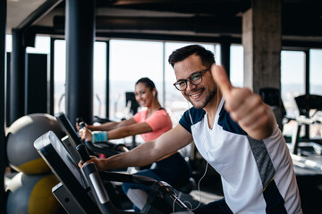 Fototapeta na wymiar Young and attractive woman and man biking in the fitness gym. They exercising legs and doing cardio workout while riding cycling machines.