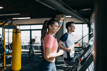 Young fit man and woman running on treadmill in modern fitness gym.