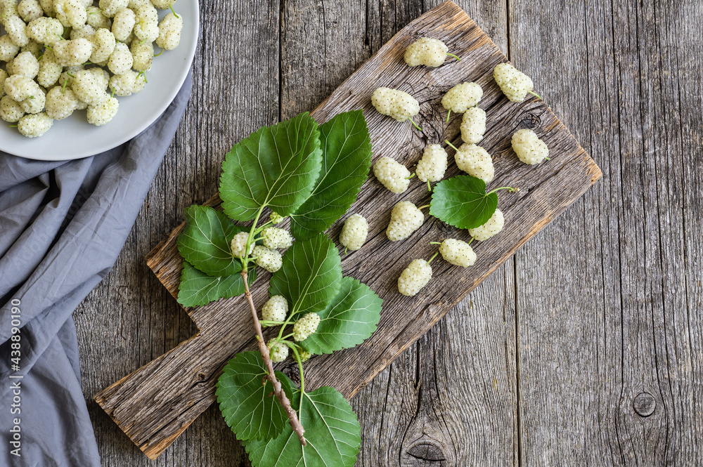 Wall mural fresh white mulberries in plate with branch on wooden background, summer fruit concept