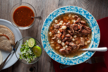 Flat lay. A plate of gallina pinta, a traditional northwest of Mexico dish with quesadillas spicy red salsa lemons onion, and cilantro over a rustic wooden table lit by a window light horizontal.