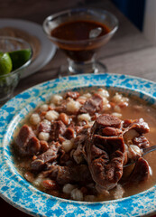 A plate of gallina pinta, a traditional northwest of Mexico dish with spicy red salsa lemons onion, and cilantro lit by a window light dark food or low key light, Mexican food, vertical.