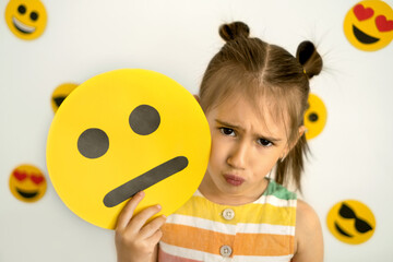 World emoji day. Anthropomorphic smile Face.  A little girl, sad with a pout, holds a cardboard sad...