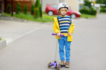 Little boy in safety helmet is riding scooter. Quality protect equipment for safety kids on street of city. Outdoor activity and leisure for children in a city.