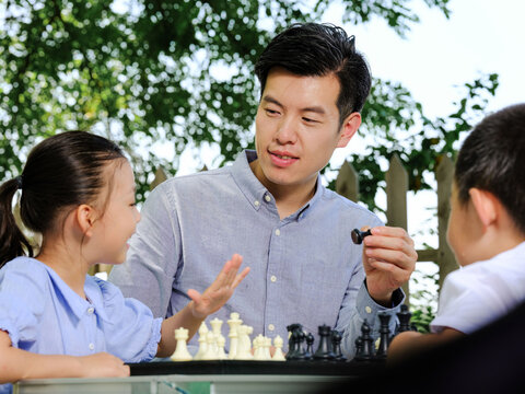 Happy family of three playing chess in the park