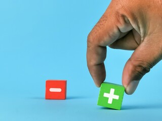 Positive and negative part concept. Hand pick and choose plus symbol on wooden cube over minus symbol.