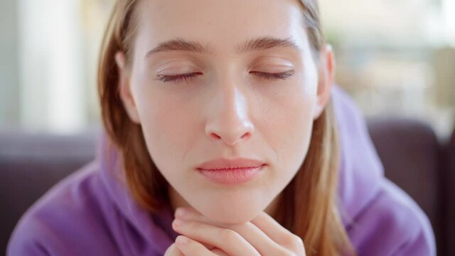 Closeup face of beautiful young woman with blue eyes looking at camera with blank facial expression and blinking, her hands on chin