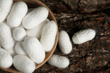 White silk cocoons with wooden bowl on tree bark, flat lay
