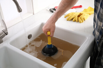 Man using plunger to unclog sink drain in kitchen, closeup - obrazy, fototapety, plakaty