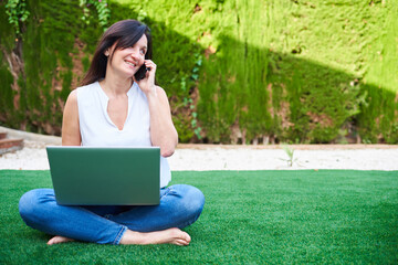 A brunette woman uses her laptop in the garden of her house